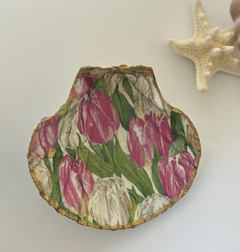 May include: A seashell with a gold trim, decorated with a pink and white floral pattern of tulips.