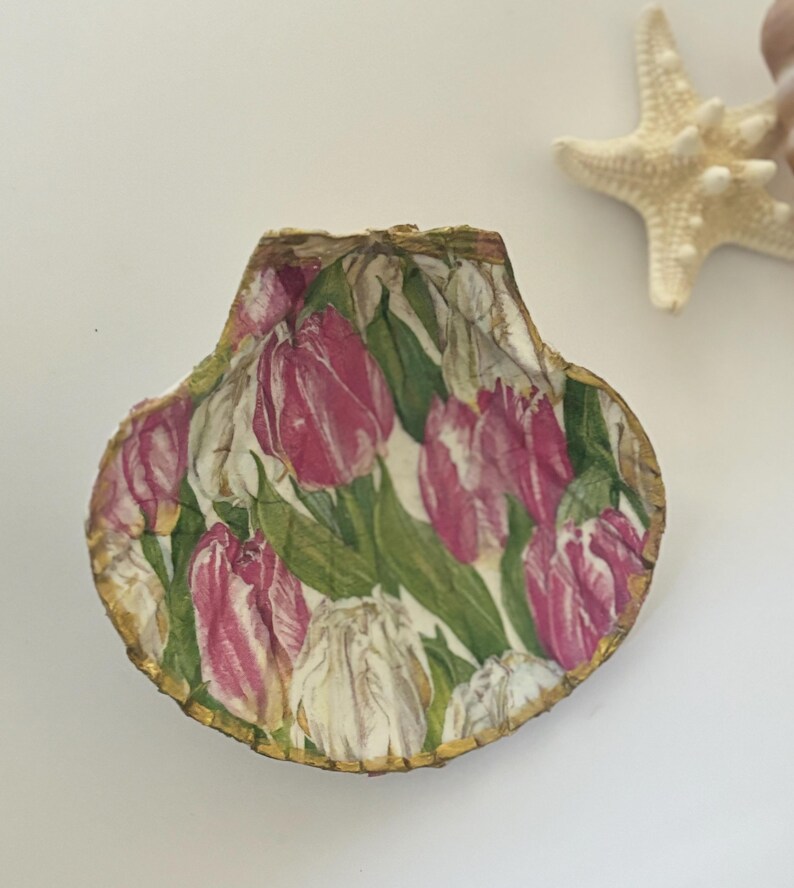 May include: A seashell with a gold trim, decorated with a floral pattern of pink and white tulips on a green background.