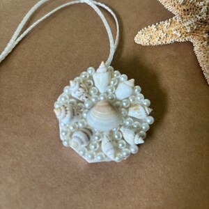 May include: A white pendant necklace with a circular design featuring a cluster of small white seashells and faux pearls.
