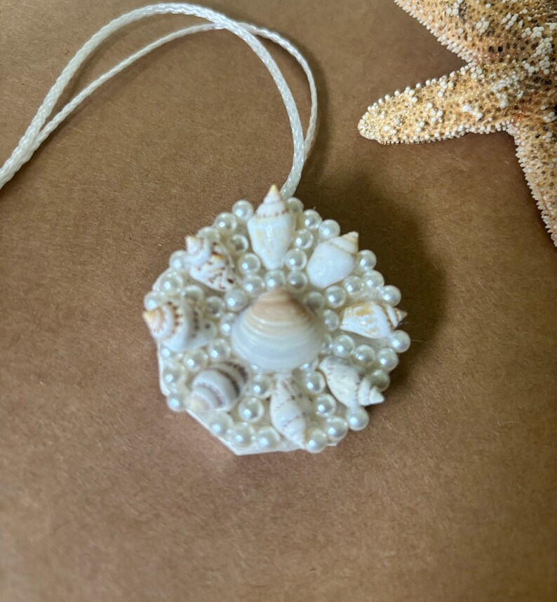 May include: A white pendant necklace with a circular design featuring a cluster of small white seashells and faux pearls.
