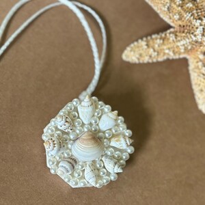 May include: A white necklace with a hexagonal pendant featuring a cluster of small white seashells and pearls.