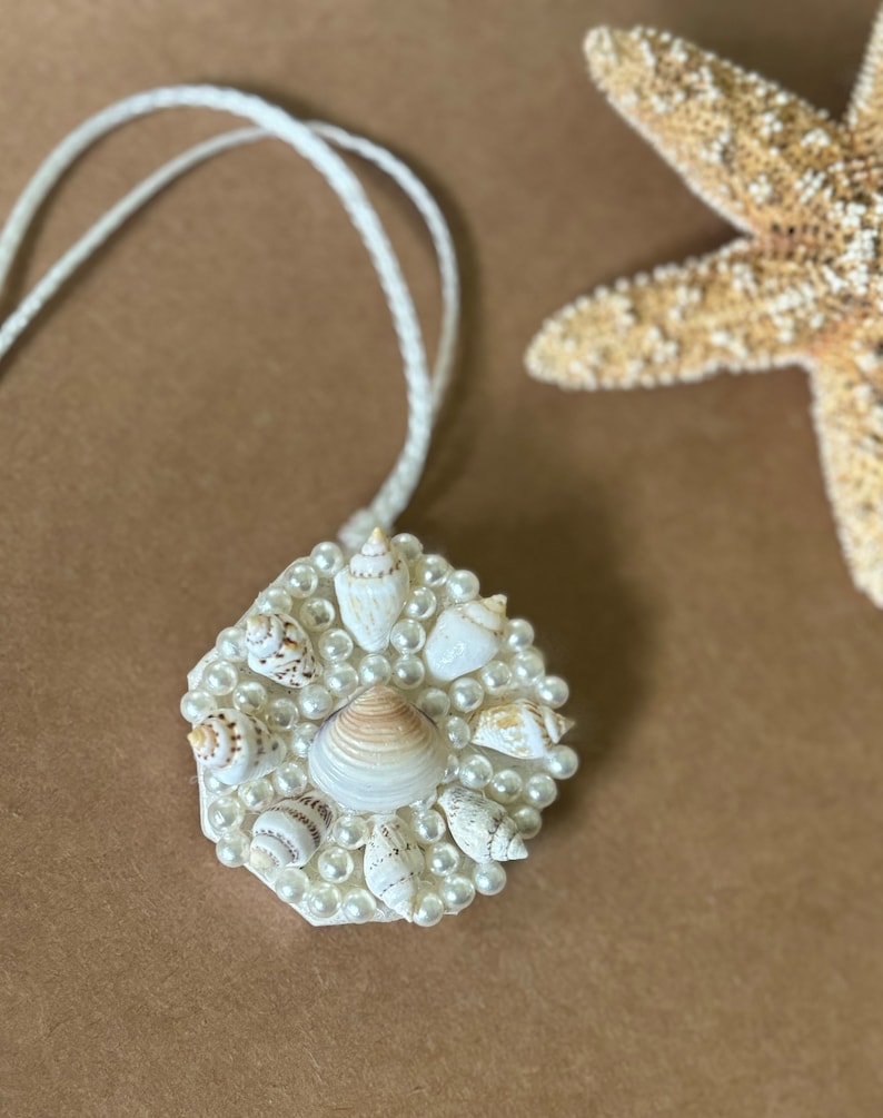 May include: A white necklace with a hexagonal pendant featuring a cluster of small white seashells and pearls.