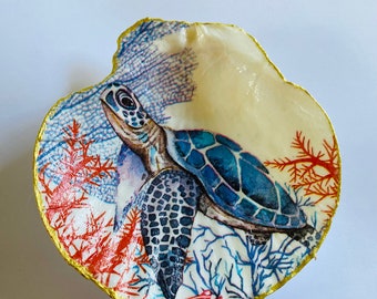 May include: A white seashell with a gold rim, painted with a blue and green sea turtle swimming through coral and seaweed.