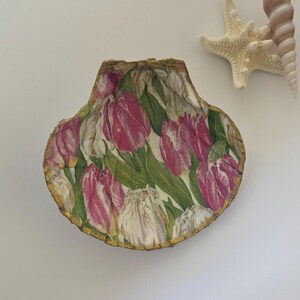 May include: A decorative seashell dish with a gold rim and a floral pattern of pink and white tulips on a green background.