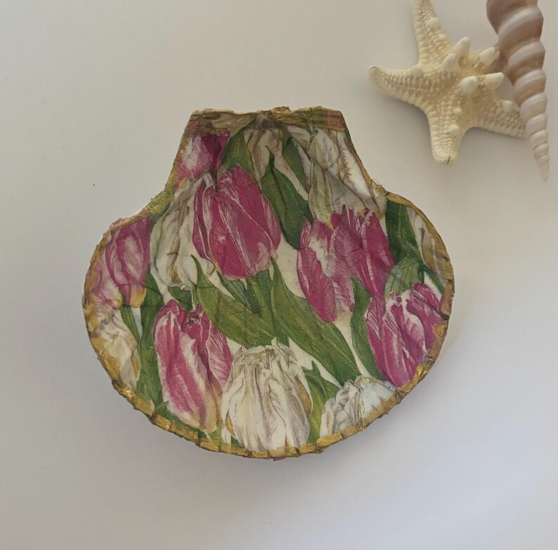 May include: A decorative seashell dish with a gold rim and a floral pattern of pink and white tulips on a green background.