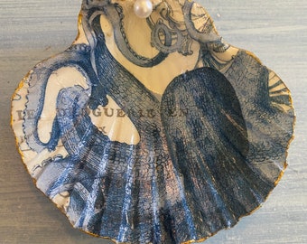 Puede incluir: Una concha de mar azul y dorada con un diseño de pulpo y una perla blanca en el centro. La concha está decorada con pan de oro y tiene un aspecto vintage.