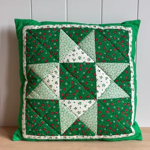 May include: A square quilted throw pillow featuring a central star pattern. The design alternates between a vibrant green fabric with small red floral prints and a white fabric with a dense green and white floral pattern, all bordered by green.