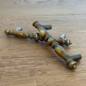May include: Antique brass cabinet handles with a decorative design. The handles have a tarnished finish, showing signs of age. The handles are approximately 5 inches long.