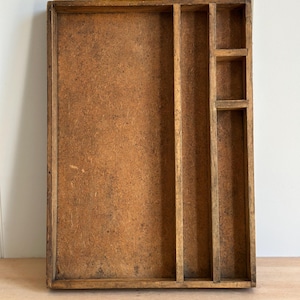 May include: A rectangular wooden organizer tray with a natural brown finish. The tray features one large open compartment on the left side, a long vertical divider, and three smaller stacked square compartments on the right side for storage.