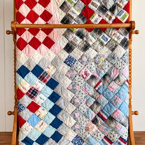 May include: A patchwork quilt featuring a diamond-patterned design made of various fabric squares in red, pink, blue, white, and black. Some squares include small floral prints, plaid patterns, and text labels reading 0404 or ID 1988.