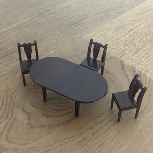May include: A miniature dark brown dining set with an oval table and three chairs. The table has four legs, and the chairs have a decorative back. The set is made of a dark brown material.