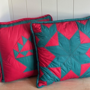 May include: Two square throw pillows featuring a quilted star pattern in alternating shades of deep red and teal green. The pillows have piped edges and a stitched geometric design, with one pillow showing a full star and the other a partial star.