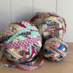 May include: Three spherical balls made of tightly wound fabric strips in various colors and patterns, including polka dots, stripes, and solid shades of pink, blue, red, and yellow. The fabric balls vary in size and feature frayed edges.