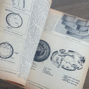May include: Open vintage manual pages with black and white diagrams and text detailing brake systems. The pages show illustrations of brake components, including drums, shoes, and springs, with labels and technical descriptions.