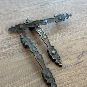 May include: A white ceramic mug with a black handle and the text "But First, Coffee" in a bold, black font. The mug is set against a blurred background, suggesting a cozy setting.