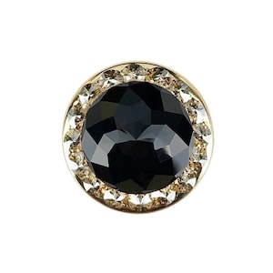 以下が含まれることがあります： 金色の枠に黒い宝石がセットされたリング。宝石の周りを透明なクリスタルが囲んでいます。