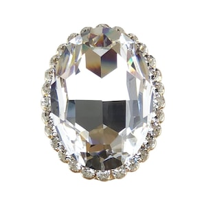 以下が含まれることがあります： 銀色の金属製の枠にセットされた、透明な楕円形のラインストーン。ラインストーンは、より小さなラインストーンの列で囲まれています。