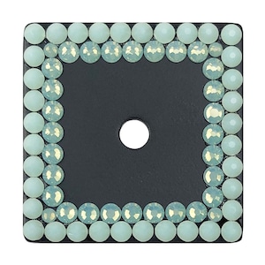 Może przedstawiać: Kwadratowy czarny skórzany łata z otworem w środku. Łata jest otoczona obramowaniem z jasnozielonych cyrkonii.