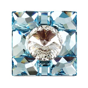 以下が含まれることがあります： 中央に大きな透明なクリスタル、周囲に小さな薄い青色のクリスタルが配置された正方形のクリスタル装飾