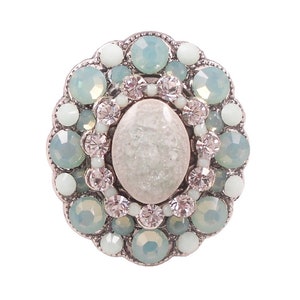 May include: A silver ring with a large oval-shaped white stone surrounded by a halo of smaller, light blue and clear rhinestones.