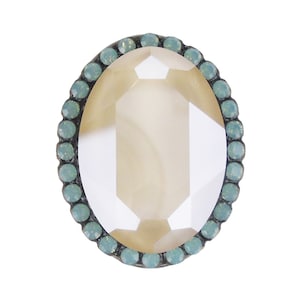 May include: A clear oval-shaped glass cabochon with a faceted design, surrounded by a border of light blue rhinestones.
