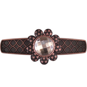 Op de afbeelding: Een decoratieve ladegreep met een zwarte en koperen afwerking. De greep heeft een bloemmotief met een helder kristal in het midden.