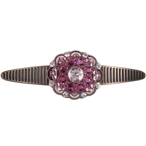 Puede incluir: Una pinza para el pelo plateada con un diseño de flor de diamantes de imitación rosa y transparente.