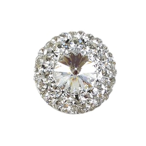 May include: A round, clear crystal rhinestone with a silver setting. The rhinestone is surrounded by a halo of smaller rhinestones.