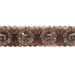 May include: A brown and silver hair clip with a decorative design of small, clear and brown rhinestones. The rhinestones are arranged in a floral pattern.