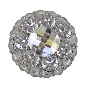 以下が含まれることがあります： 中央に大きなファセットカットのクリスタルが置かれ、その周りを小さなクリスタルが囲む銀色のボタン。ボタンは円形で、装飾的なビーズの縁があります。