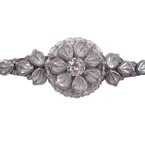 Może przedstawiać: Srebrna spinka do włosów z kwiatowym wzorem. Środek kwiatu to przezroczysty kryształ górski. Spinka jest wykonana z metalu i ma błyszczące wykończenie.