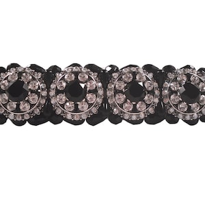 Könnte beinhalten: Schwarzes Armband mit drei runden schwarzen Steinen, die von klaren Strasssteinen umgeben sind.