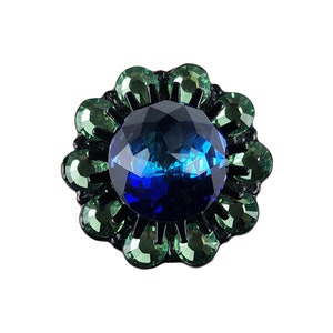 Peut inclure: Une broche en forme de fleur avec un grand cabochon bleu au centre, entouré de pierres vertes et bleues.