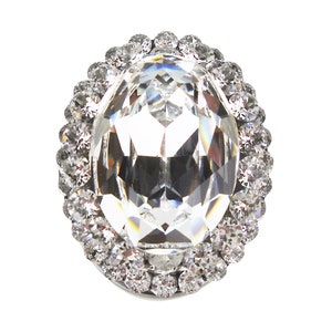 以下が含まれることがあります： 小さな透明なクリスタルで囲まれた大きな透明なクリスタルオーバル。クリスタルはファセットカットされており、光を反射しています。