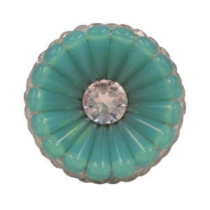 May include: A turquoise blue glass flower with a clear rhinestone centre. The flower is surrounded by a clear glass border.
