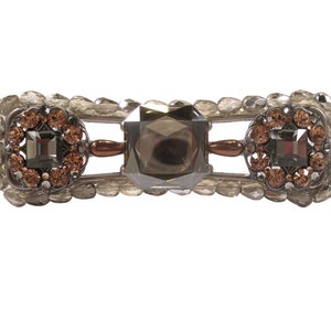 Könnte beinhalten: Eine silberne Haarklammer mit drei großen, facettierten, dunkelgrauen Kristallen. Die Kristalle sind von kleineren, hellbraunen Kristallen umgeben.