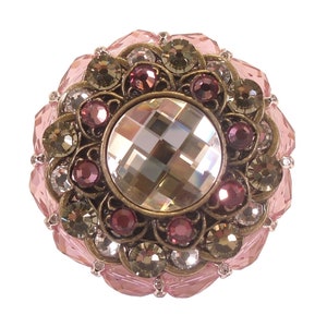 Könnte beinhalten: Ein runder, rosafarbener und goldener Schmuckstein mit einem großen, klaren Kristall in der Mitte. Der Schmuckstein ist von kleineren Kristallen in Rosatönen und Gold umgeben.