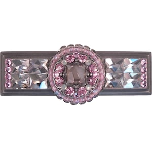 Könnte beinhalten: Ein silberner Schubladenknauf mit einem rosa Kristallbesatz. Der Knauf hat eine rechteckige Basis mit einem quadratischen Kristall in der Mitte. Der Kristall ist von einem Kreis aus kleineren rosa Kristallen umgeben.