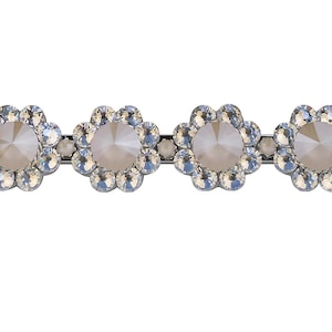 Op de afbeelding: Zilverkleurige haarspeld met vier bloemvormige versieringen. Elke bloem heeft een grote, facetgeslepen, lichtgekleurde middensteen, omringd door kleinere, heldere kristallen. Ontworpen voor haarstyling.