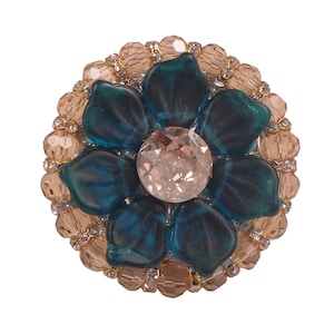 以下が含まれることがあります： ゴールドとベージュのビーズの輪で囲まれた、大きな透明なラインストーンの中心を持つ、ターコイズブルーの花です。