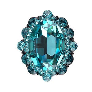 以下が含まれることがあります： ターコイズブルーの大きな楕円形の宝石が、小さな輝くターコイズブルーの宝石のハローで囲まれたリングです。