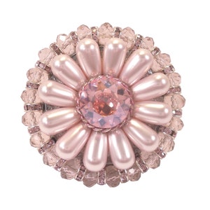 以下が含まれることがあります： 中央に大きなピンク色のクリスタル、縁に小さなピンク色のクリスタルが円形に並んだ、ピンクの花のブローチです。