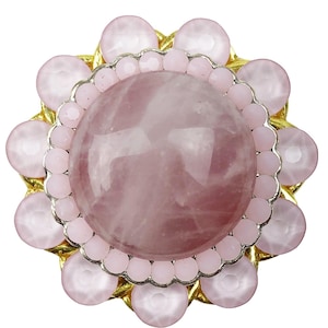 May include: A round, light pink gemstone ring with a gold-colored metal base. The ring features a large, central rose quartz stone surrounded by smaller, pink, bead-like stones and a gold-colored metal border. The design is floral-inspired.