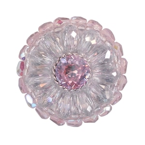 以下が含まれることがあります： 中央に大きなピンク色のクリスタルがついた、ピンクと透明なクリスタルでできた花のブローチです。