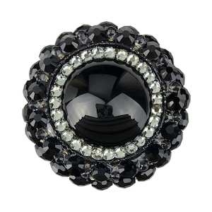 以下が含まれることがあります： 黒いボタン。丸い黒い中心に、透明なラインストーンのリングと、黒いラインストーンの縁取りが施されています。