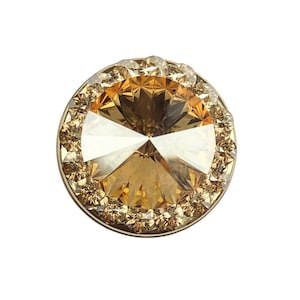 May include: A round, gold-toned, crystal embellishment with a clear, faceted center and a border of smaller, clear crystals.