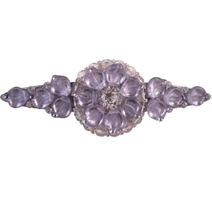 Op de afbeelding: Een zilveren haarspeld met een groot paars bloemenontwerp. De bloem is gemaakt van meerdere kleine paarse bloemblaadjes met een heldere strasssteen in het midden.
