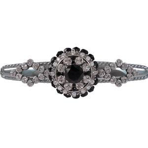 以下が含まれることがあります： 黒と白のラインストーンのデザインが施されたシルバーのヘアクリップ。クリップは装飾的で華やかなデザインです。