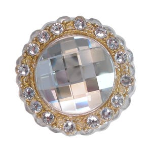 以下が含まれることがあります： 透明なラインストーンで囲まれた、透明なファセットカットのクリスタルの中心を持つ、丸い金色の装飾的な作品です。