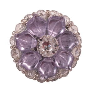 Puede incluir: Un broche de flor púrpura con un centro de cristal de roca transparente rodeado de cuentas transparentes.
